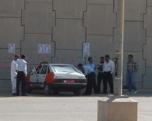 A man peers into a small red and white taxi as six other men stand nearby